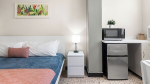 Hotelkamer met een bed, nachtkastje met lamp, magnetron, koelkast en een kleine potplant.