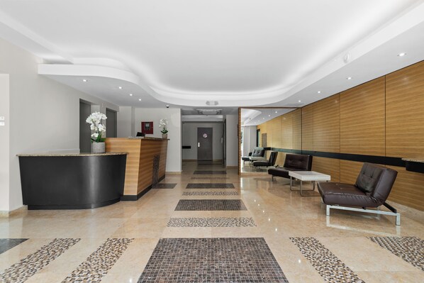 A modern reception area with a curved reception desk, a seating area with a sofa and chairs, and a patterned floor. - Steps From La Placita Coffee Parking AC (San Juan)