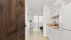 Une cuisine moderne avec des meubles blancs, une porte en bois et une vue sur un balcon.