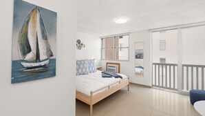 Une chambre à coucher avec un lit, un tableau représentant un voilier, une fenêtre et un balcon.