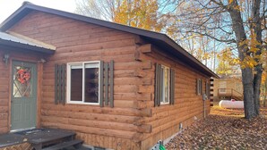 A wooden cabin with a front porch, a door with a wreath, and a window with shutters. - Rustic UP Waterfront Cabin on Huron Bay (L'Anse)
