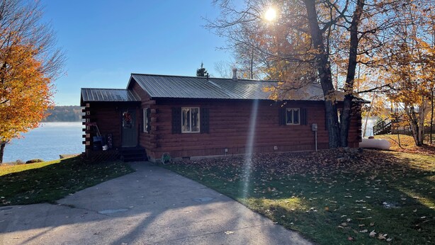 A wooden cabin with a metal roof, a visible chimney, and a door with a green frame. - Rustic UP Waterfront Cabin on Huron Bay (L'Anse)