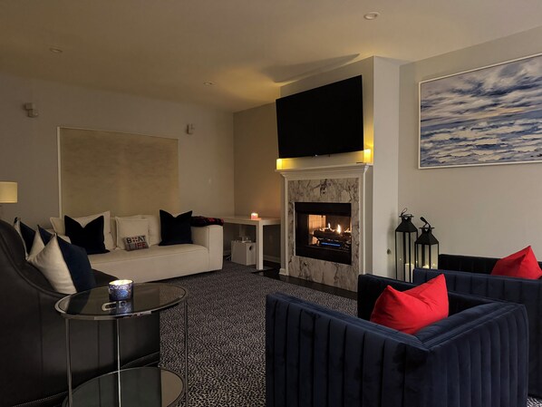 A modern living room with a fireplace, a sofa, a coffee table, and a TV mounted on the wall. - Luxurious Lakefront Retreat – Sleeps 11 (Newtown)