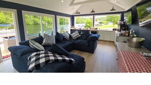 A spacious living area with large windows, a sofa set, and a kitchen area. - Luxurious Lakefront Retreat –  Sleeps 11 (Newtown)
