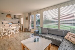 Een moderne keuken met witte kasten, een eettafel met stoelen en een grijze bank met kussens.