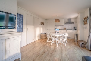 A modern kitchen with white cabinets, a dining table with chairs, and a television mounted on the wall.