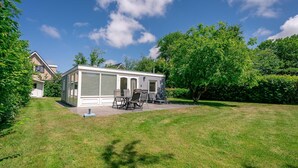 A single-story house with a covered patio area, a lawn, and trees in the background. - Cozy Detached Bungalow for 4 Persons (De Koog)