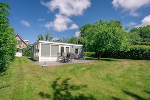 A single-story house with a covered patio area, a lawn, and trees in the background.