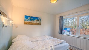 A bedroom with a bed, a window with curtains, a painting on the wall, and a radiator. - Cozy Detached Bungalow for 4 Persons (De Koog)