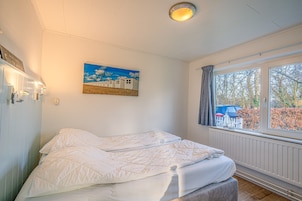A bedroom with a bed, a window with curtains, a painting on the wall, and a radiator.