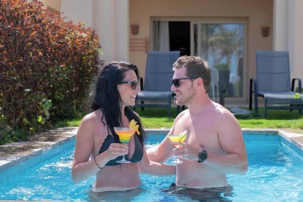 Two people in a swimming pool holding drinks.