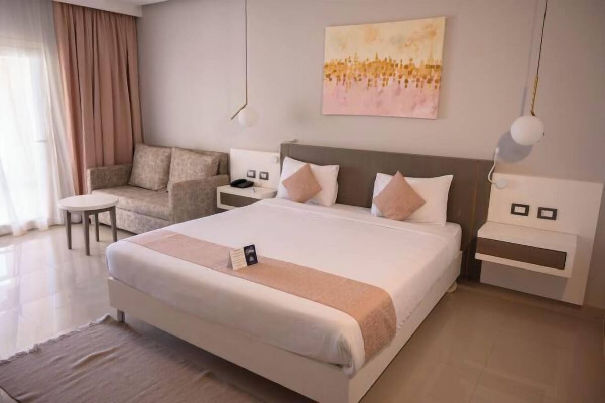 A hotel room with a large bed, a sofa, a small table, and a painting on the wall.