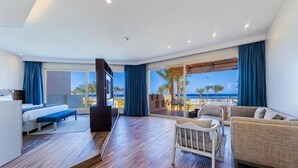 A hotel room with a bed, a sofa, a TV, a dining table, and a view of the beach. - Sataya Resort Marsa Alam (Qesm Marsa Alam)