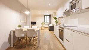 A modern kitchen with white cabinets, a built-in microwave, and a wooden dining table with chairs. - Bravissimo Força 17 Pedra, Studio Apartment (Girona)