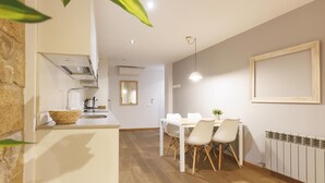 Una cucina moderna con mobili bianchi, forno integrato e un'isola grande. C'è un'area pranzo con tavolo e sedie bianche e un termosifone a parete.