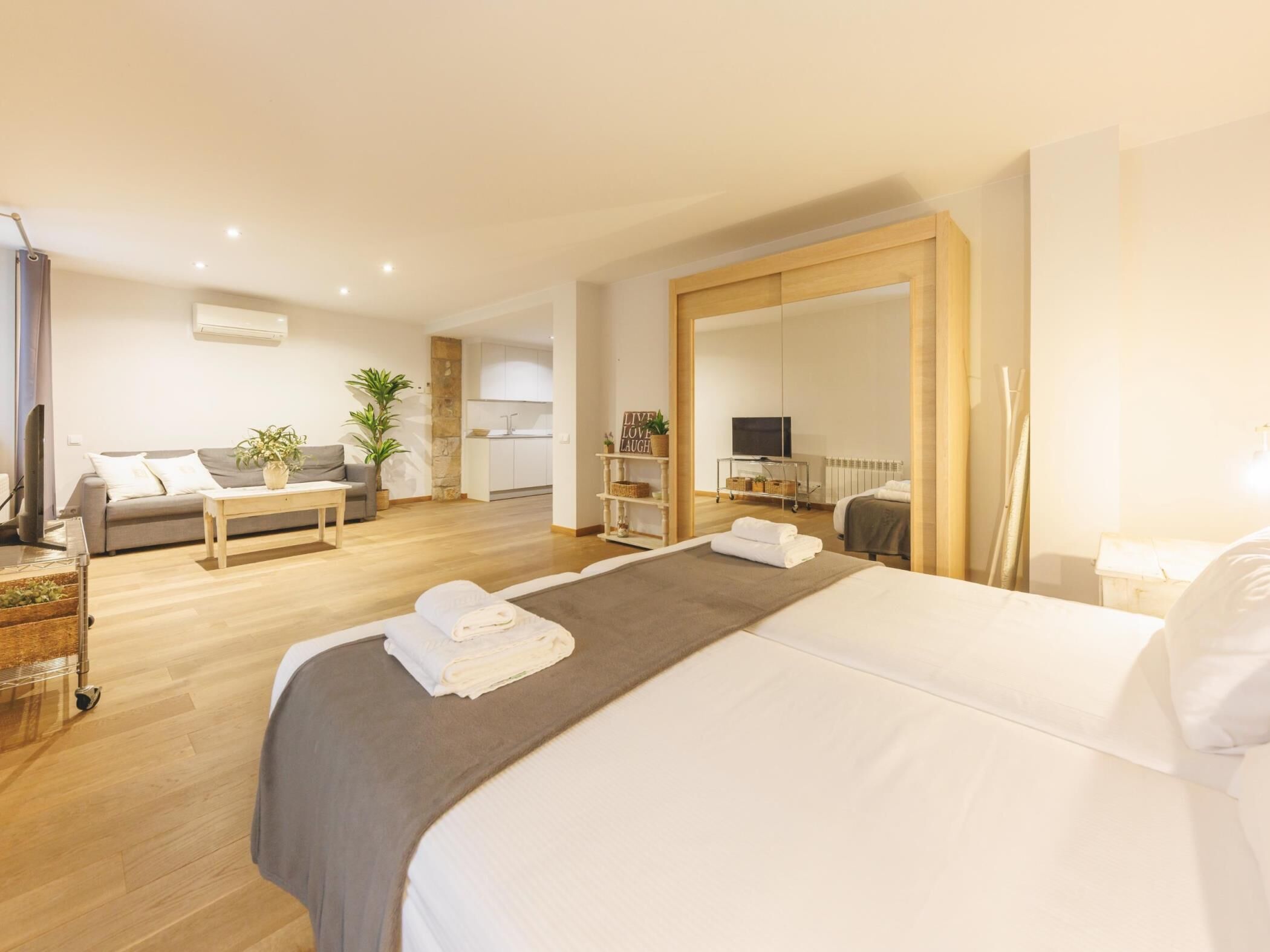 Een moderne hotelkamer met een groot bed, een bank, een klein keukenhoekje en een grote spiegel.