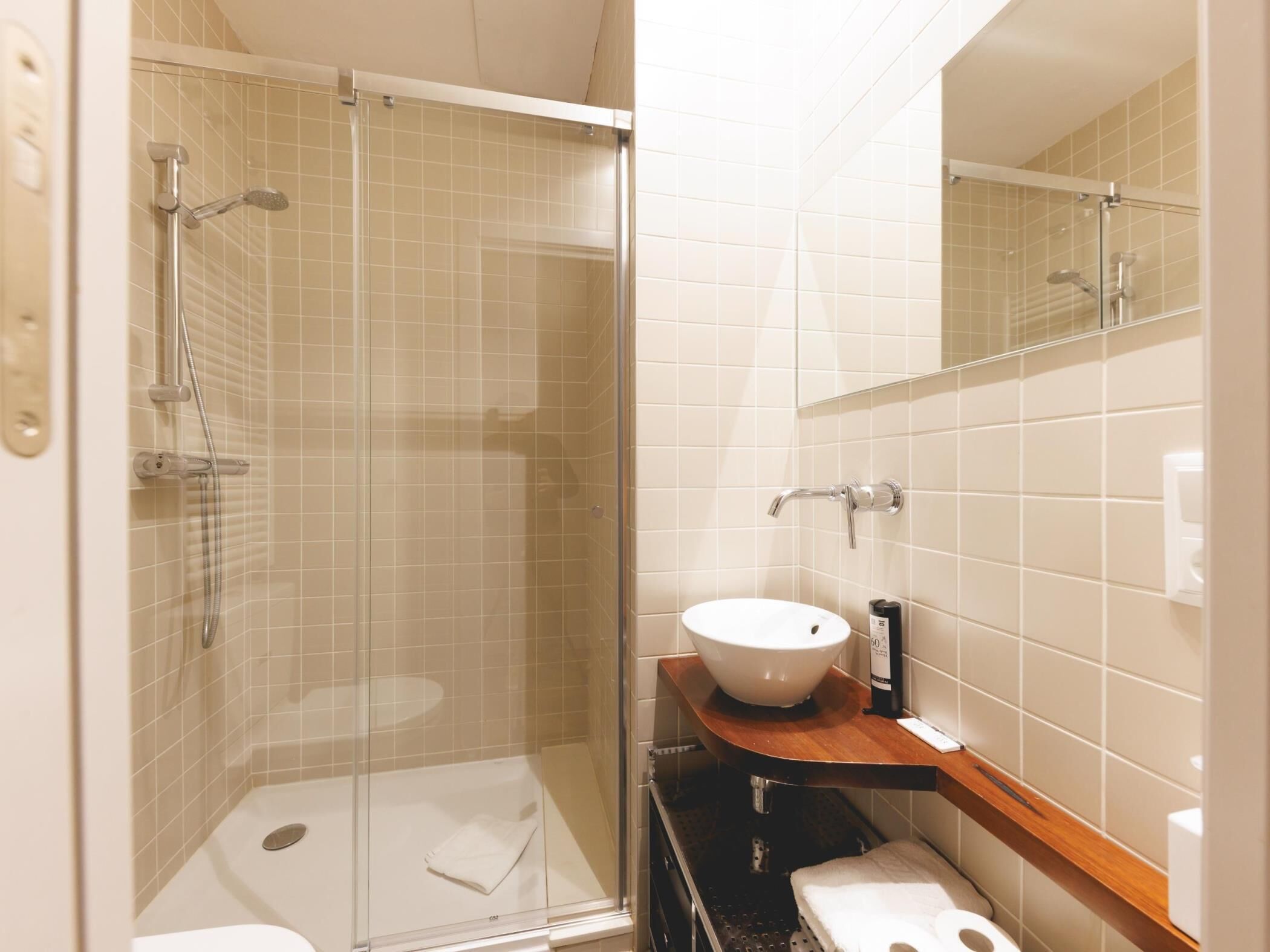 A modern bathroom with a glass-enclosed shower, a white sink, and a wooden vanity.