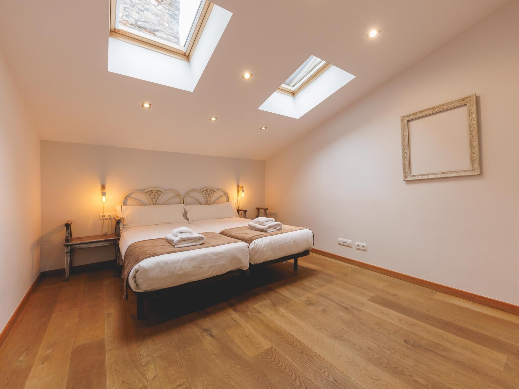 Une chambre à coucher avec un grand lit, deux tables de chevet, une lucarne et un tableau encadré au mur.