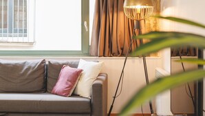 En hyggelig stue med sofa, gulvlampe og et vindue med gardiner.