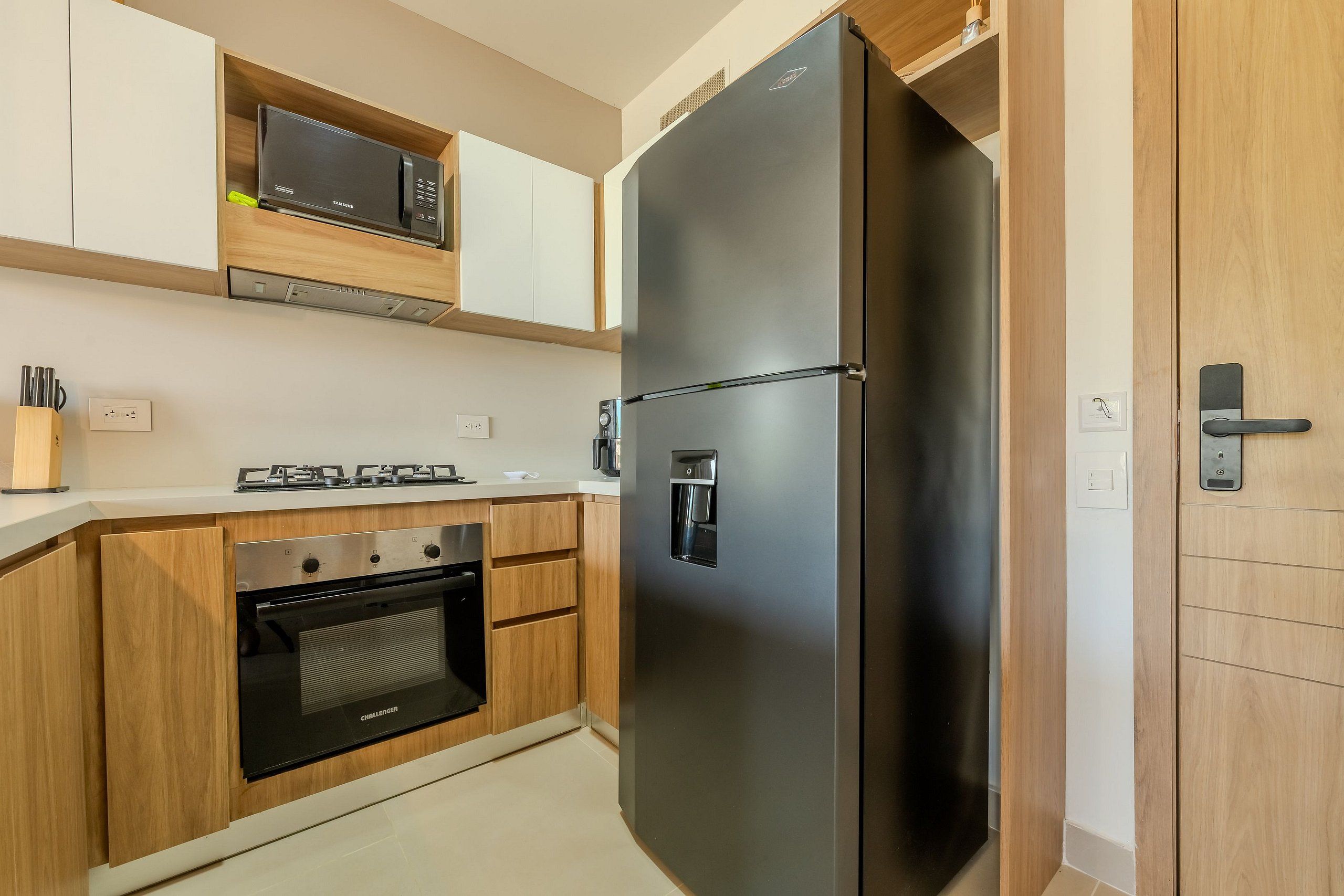 Una cocina moderna con refrigerador de acero inoxidable, horno empotrado, microondas y muebles de madera.