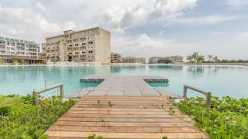 Een houten steiger die uitkomt bij een helder zwembad, met uitzicht op hotelgebouwen en palmbomen.
