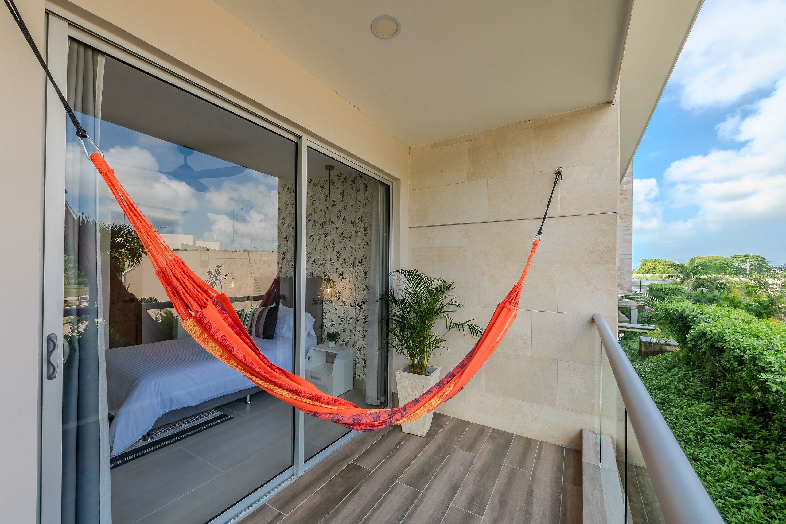 A balcony with a hammock, a bed, and a potted plant.