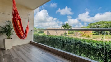A balcony with a red hammock, a potted plant, and a view of a green landscape with trees and a building.