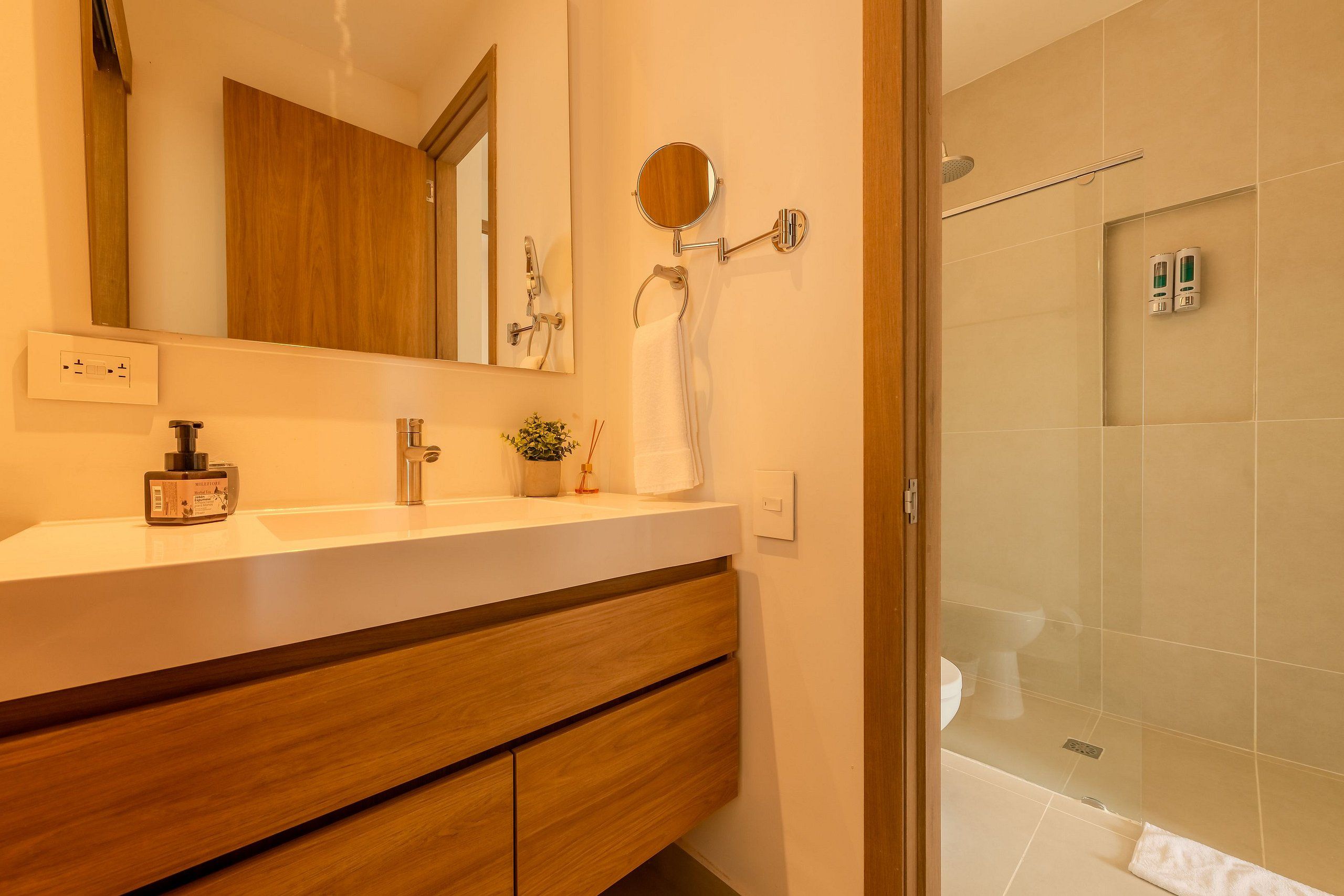 Een moderne badkamer met een houten wastafelmeubel, een spiegel, een handdoekrek en een douchegedeelte.