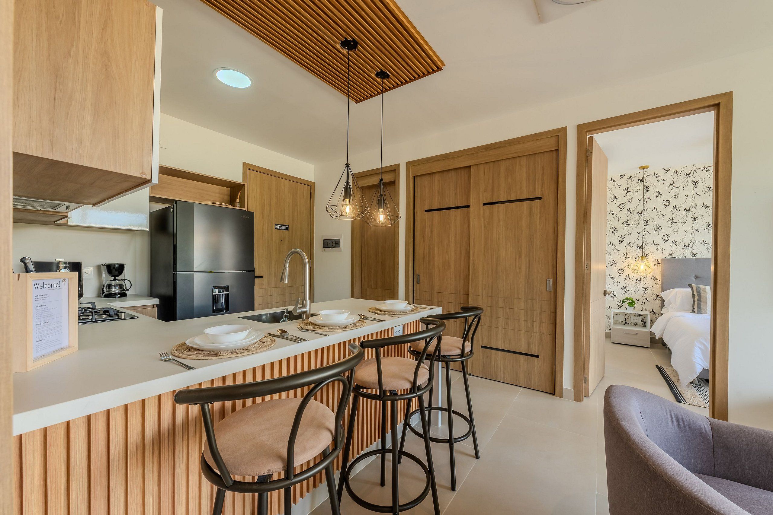 A modern kitchen with a central island, bar stools, wooden cabinets, and a wooden ceiling.