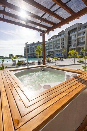 A wooden deck with a hot tub, overlooking a beach and a hotel building. - Apartamento premium en Baia Kristal (Cartagena)