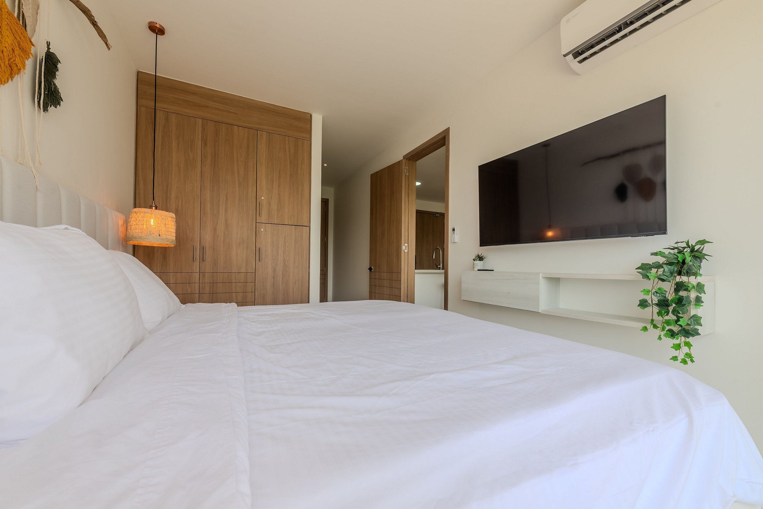 Quarto com cama grande, guarda-roupa de madeira e televisão fixada na parede.