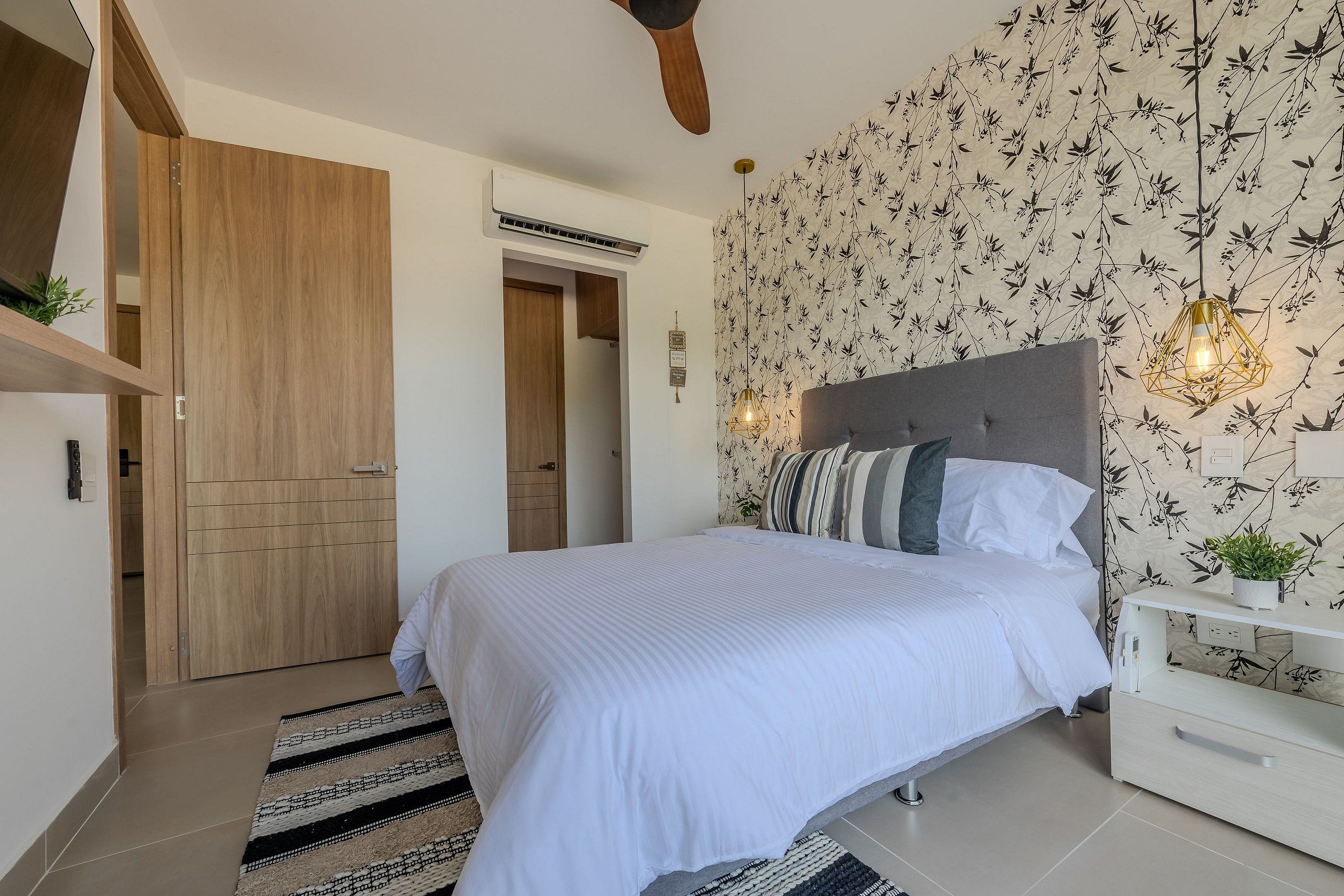 A bedroom with a bed, a nightstand, a wooden wardrobe, and a wall with a floral pattern.
