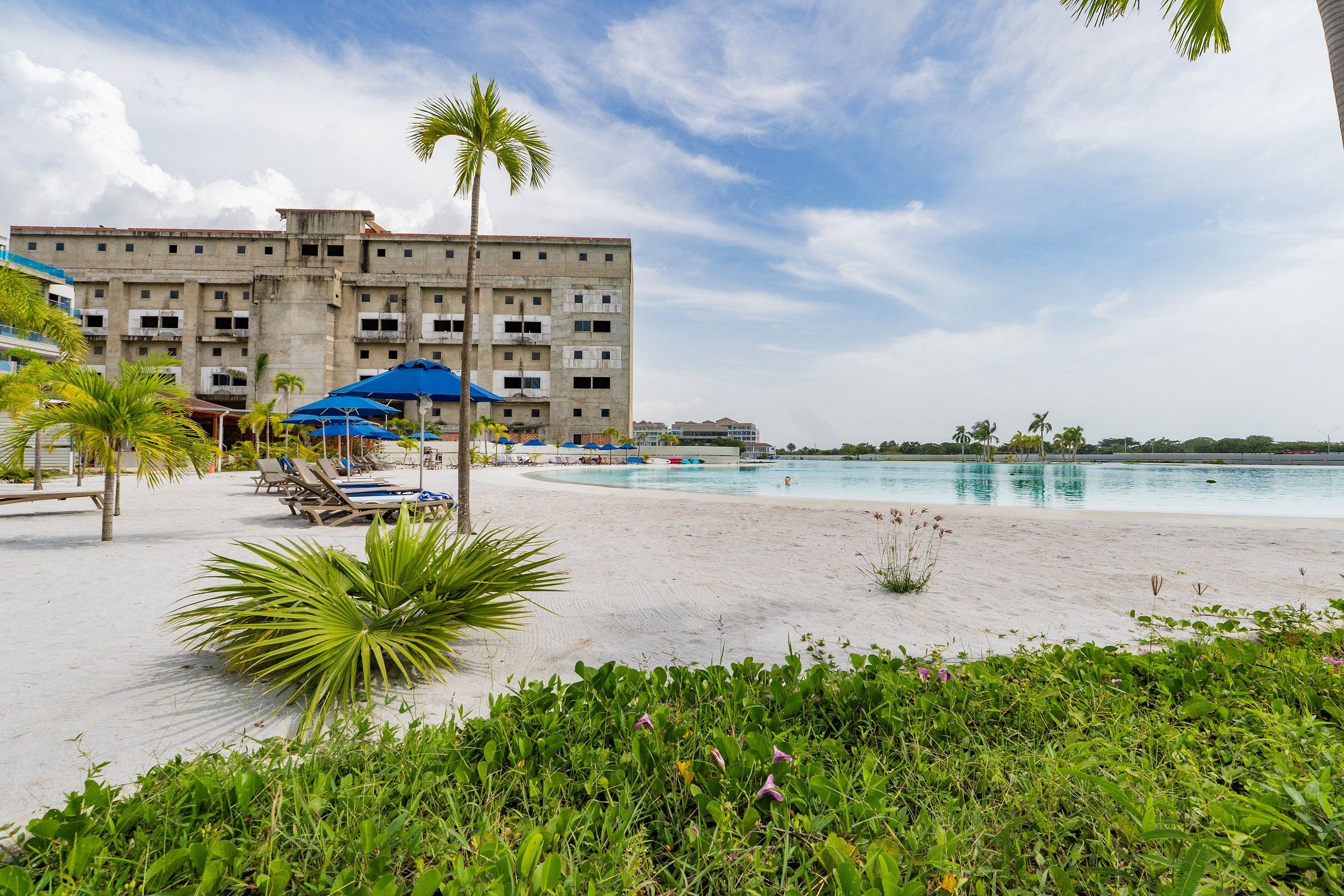 Ein Hotel am Strand mit Pool, Palmen und Liegestühlen.