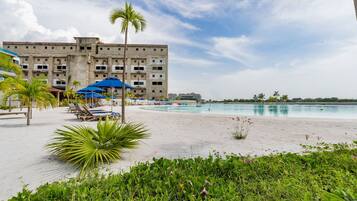 Ein Hotel am Strand mit Pool, Palmen und Liegestühlen.