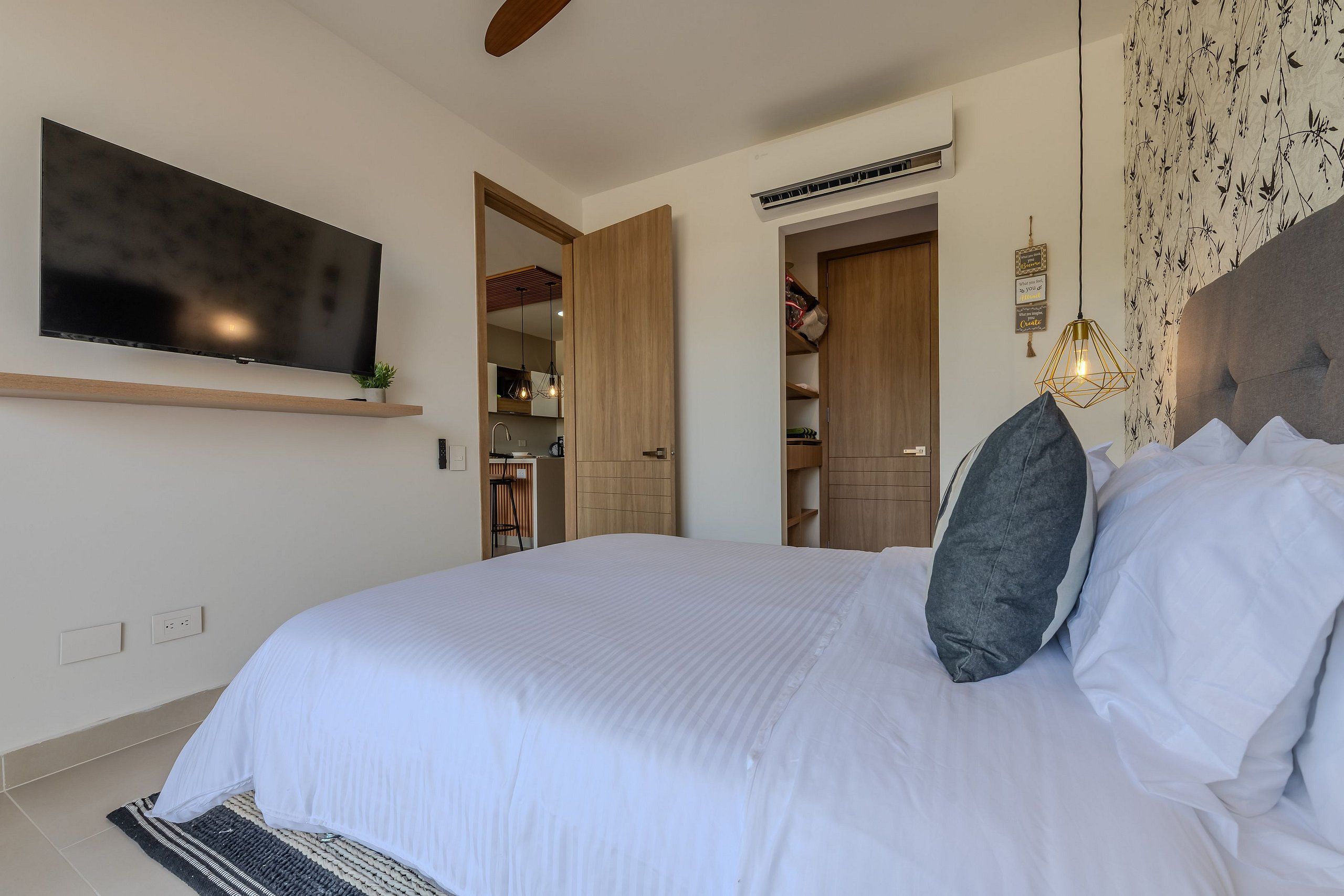 Een slaapkamer met een groot bed, een aan de muur bevestigde televisie en een kledingkast.