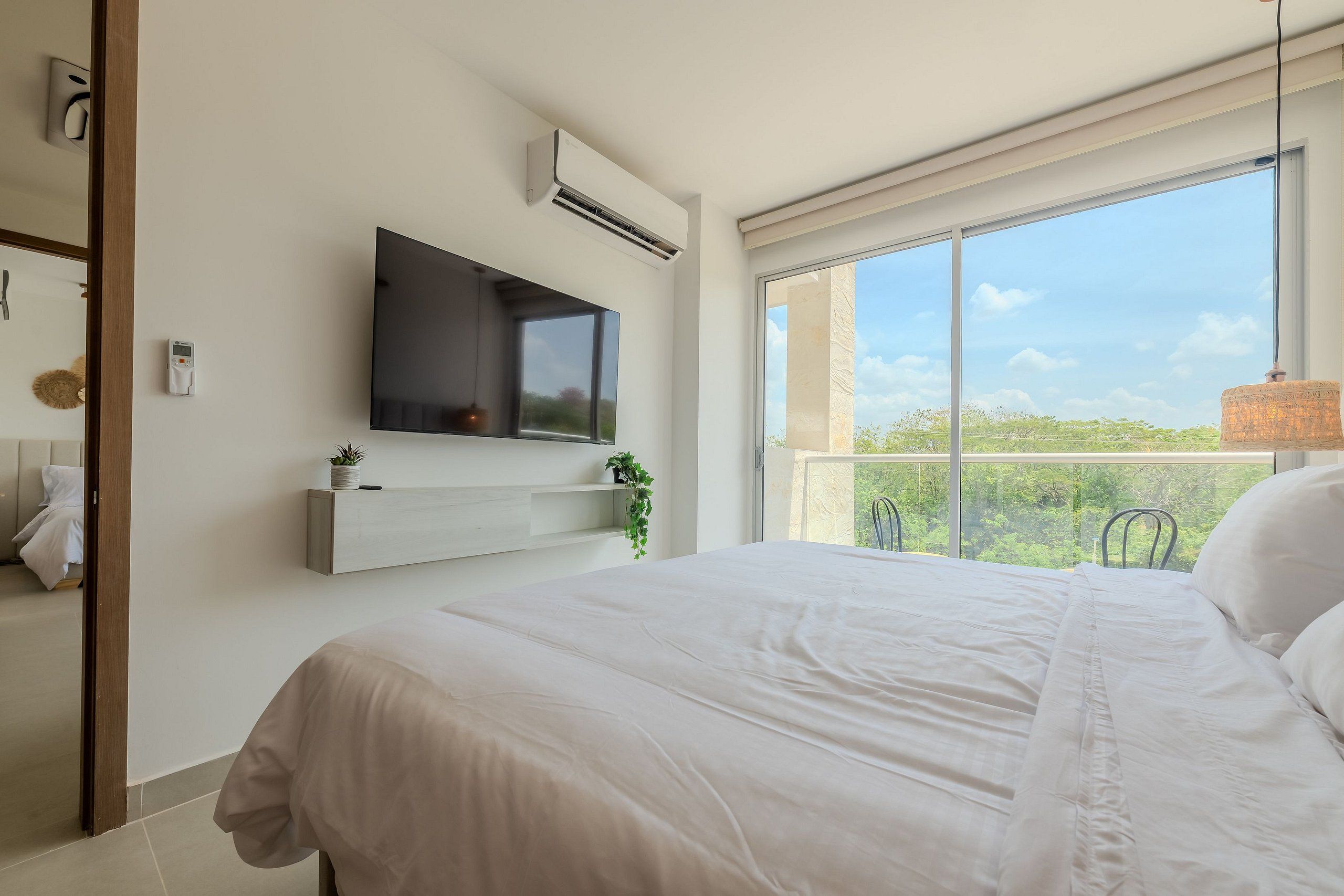 Un dormitorio con una cama grande, televisor montado, aire acondicionado y ventana con vistas a zonas verdes.