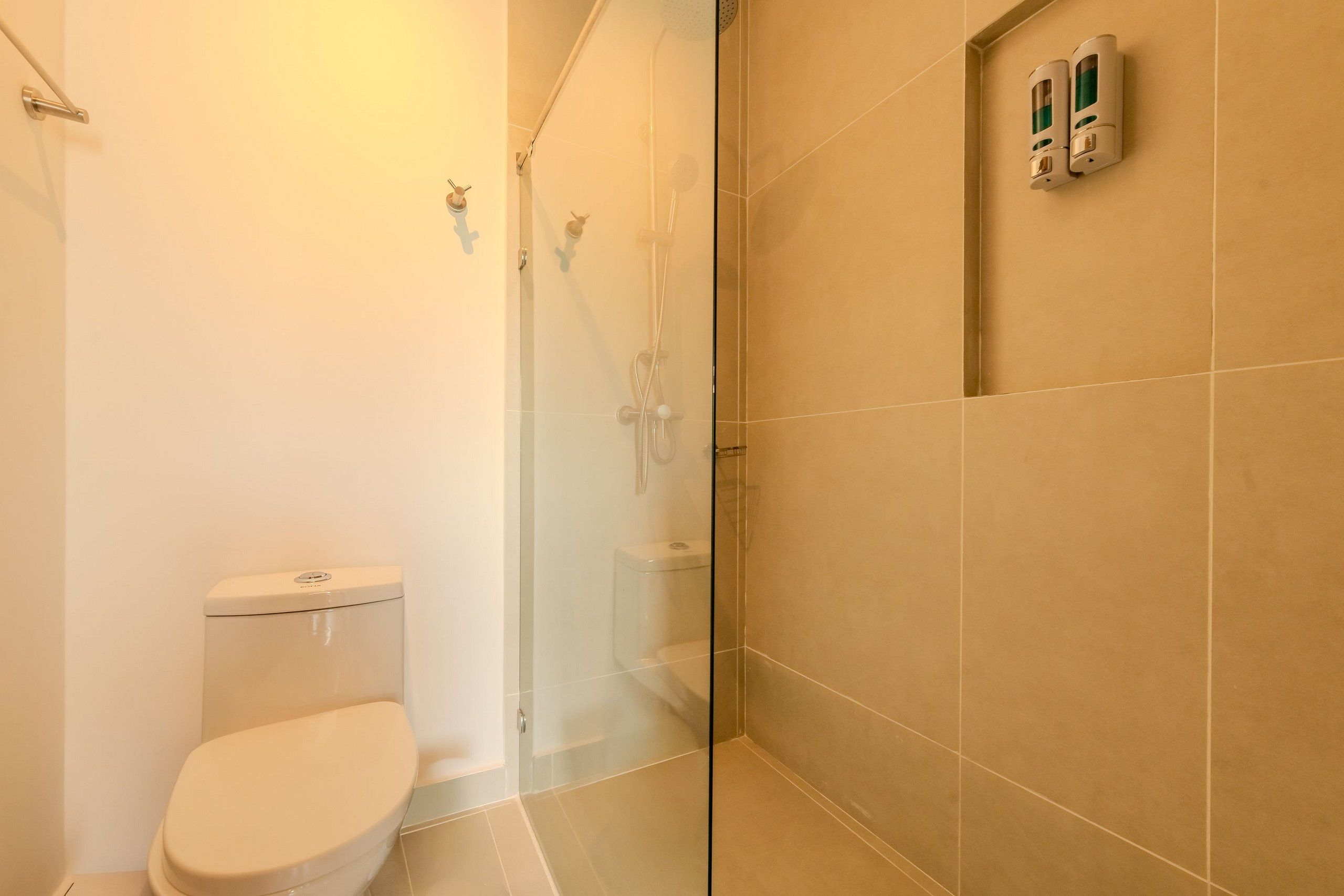 Ein Badezimmer mit Toilette, einer gläsernen Duschkabine und einem wandmontierten Seifenspender.