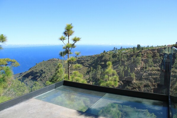 A modern glass balcony with a clear view of a mountainous landscape and the sea.