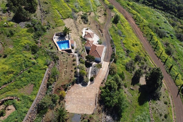 Vista aérea de una propiedad con piscina, una casa de techo a lajas y un camino de entrada pavimentado.