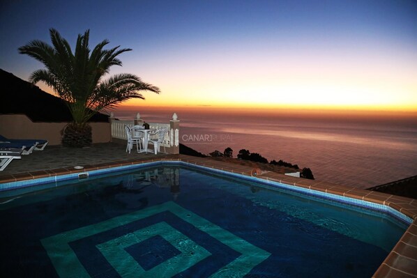 A swimming pool with a sunset view, a palm tree, and a white fence. - Private pool, jacuzzi and sea views (Puntagorda)
