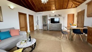 Ein Wohnzimmer mit Sofa, Couchtisch, Fernseher und einem Essbereich mit Stühlen und Tisch.