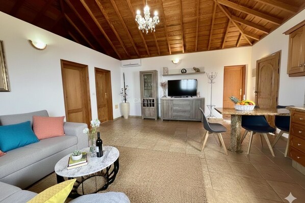 A living room with a sofa, a coffee table, a television, and a dining area with chairs and a table. - Private pool, jacuzzi and sea views (Puntagorda)