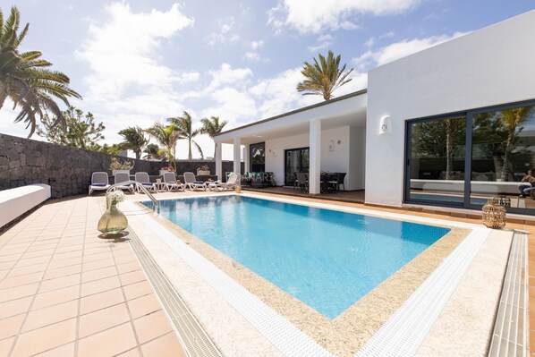 A modern outdoor pool area with lounge chairs, a stone wall, and palm trees.