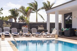 A pool area with lounge chairs, a stone wall, and a building with a sign that reads 'CANARI'.
