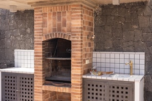 A brick-built outdoor kitchen with a built-in grill, a sink, and a tiled backsplash.