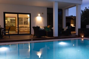 Une piscine entourée de parois en verre, un coin repas avec des chaises et une cheminée.