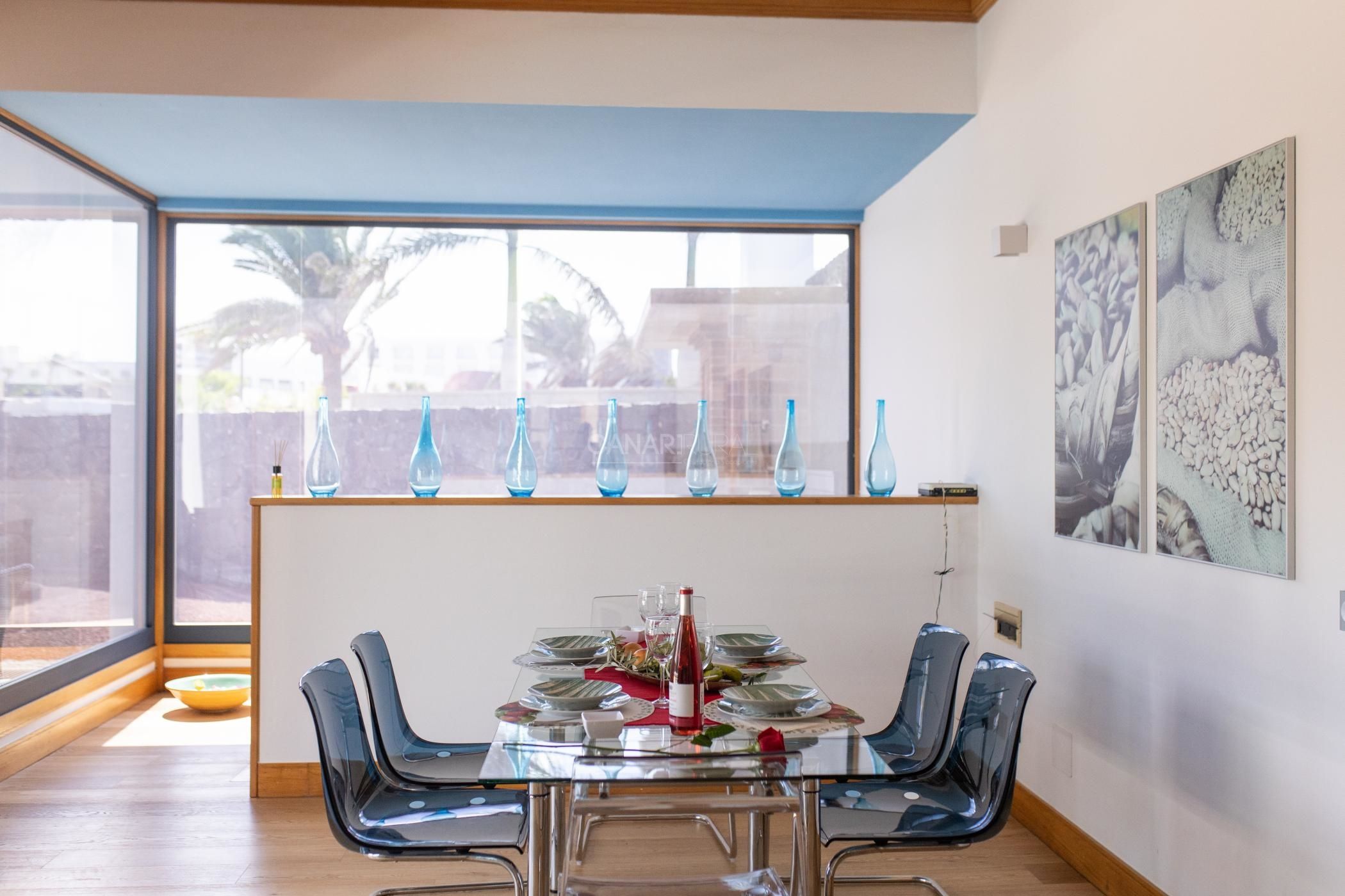 Un espace repas avec une table en verre, des chaises bleues et une vue dégagée grâce à de grandes fenêtres.