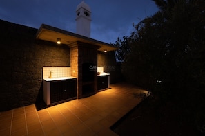 A brick exterior with a white tower-like structure, a tiled floor, and a small outdoor kitchen area.