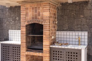 Una cocina al aire libre de ladrillo con una parrilla integrada, un lavamanos y un salpicadero de azulejos.