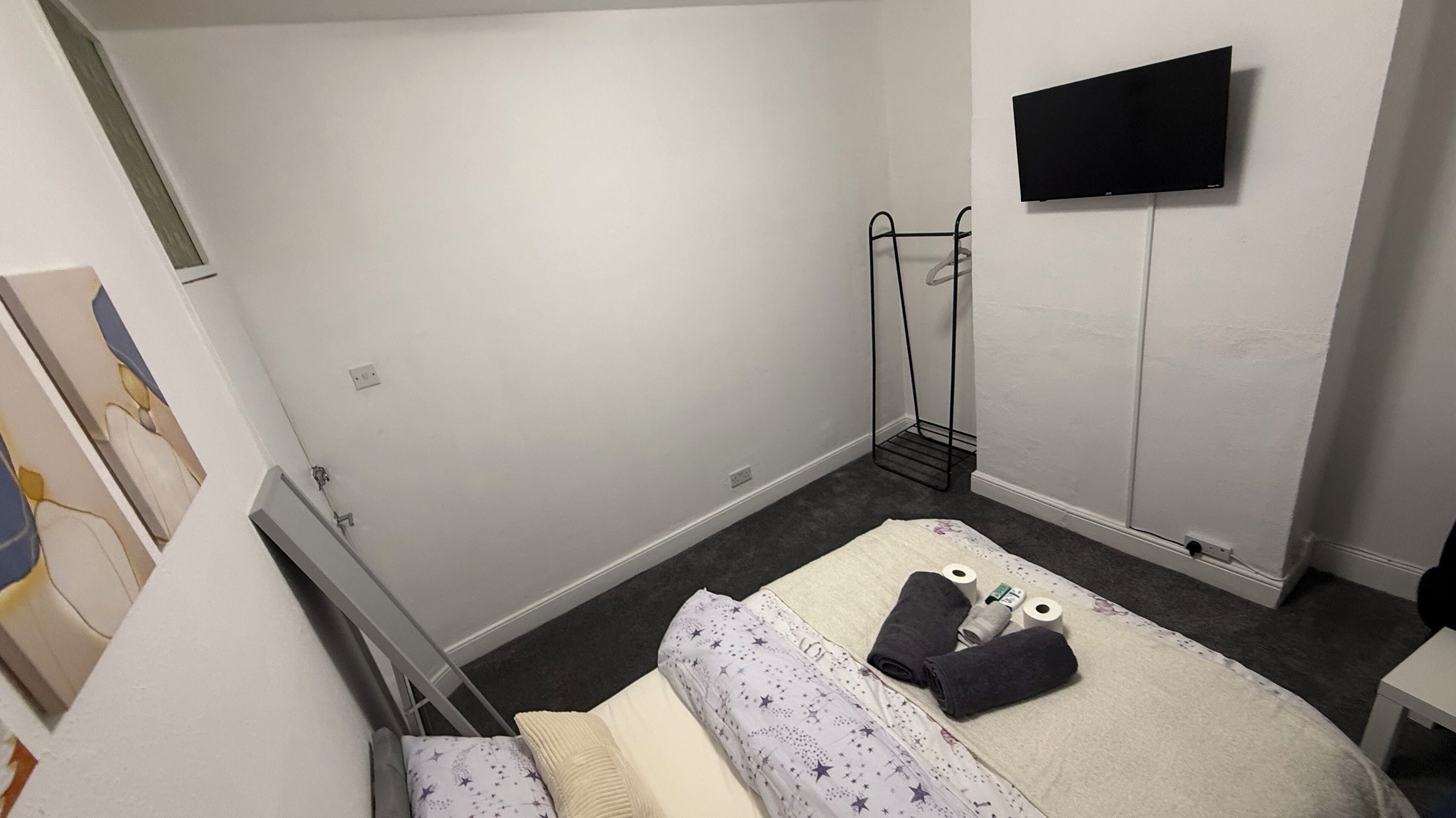 Ein kleines, einfach eingerichtetes Zimmer mit einem Bett, einem an der Wand befestigten Fernseher und einer Heizung.